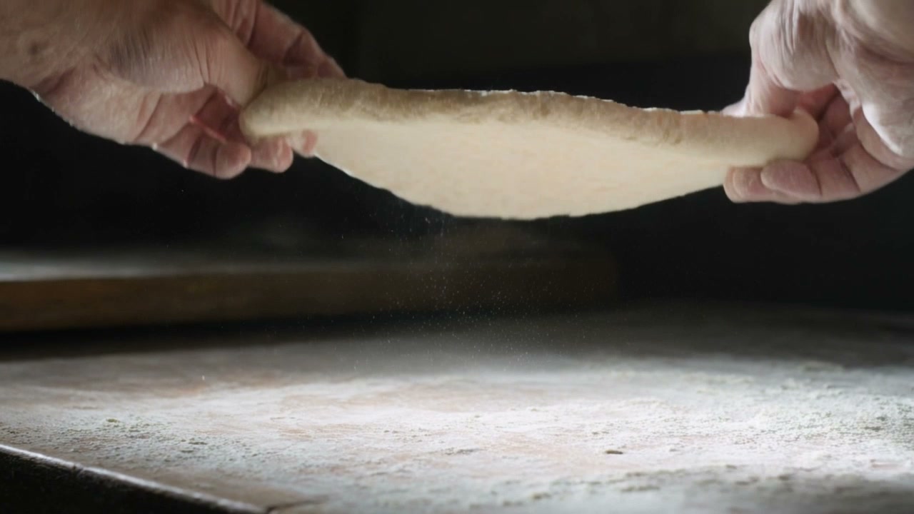 Hands pressing fresh pizza dough in a drift of flour at Rag Rug